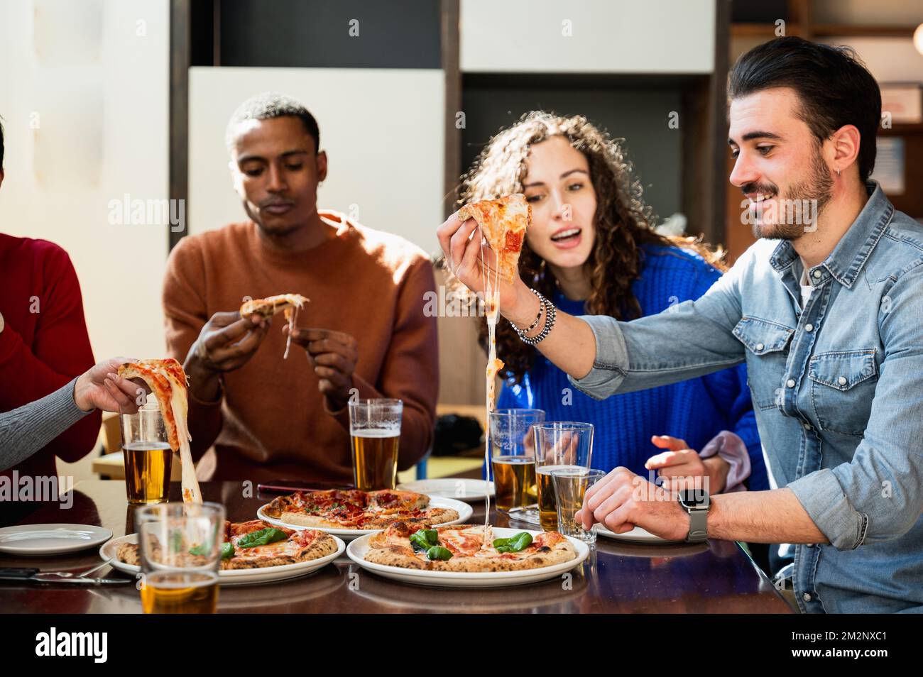 Multiethnische Gruppe von Freunden, die am Tisch sitzen und essen. Die Pizzastücke haben feinen Käse. Italienischer Lebensstil Stockfoto