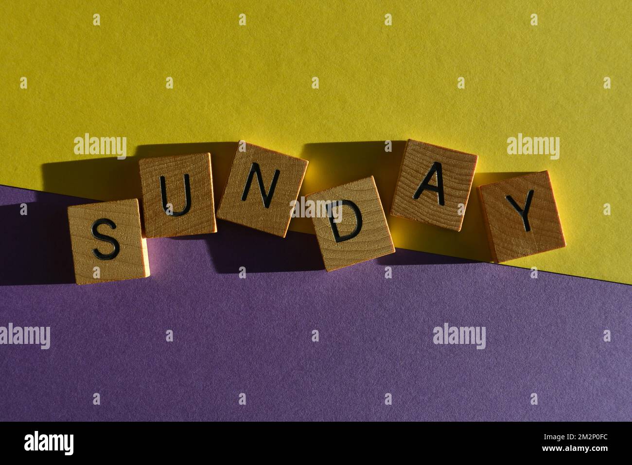 Sonntag, Wort in hölzernen Buchstaben isoliert auf hellem gelben und lila Hintergrund Stockfoto