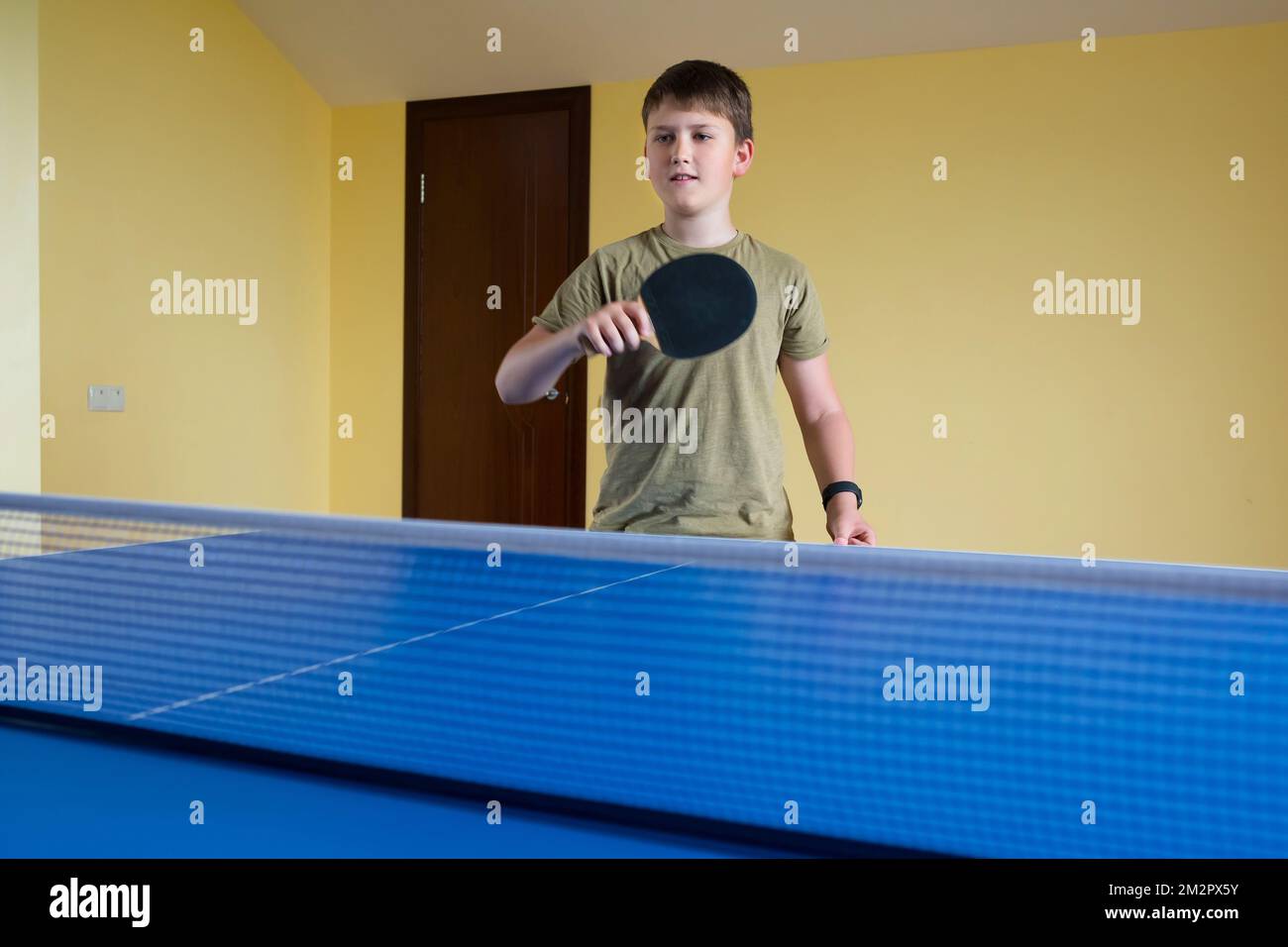 Ein 11-jähriger Teenager mit einem Tennisschläger in der Hand spielt Ping Pong. Sportlicher Lifestyle Stockfoto