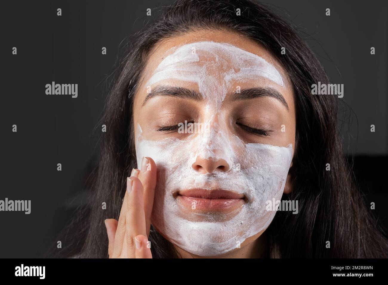 Verschlossene Augen mit Tonmaske. Kaukasisches Mädchen, das zu Hause Spa macht, Schönheitsbehandlungen Konzept Ideenbild. Sie hat ihre Wange sanft berührt. Hautpflege. Stockfoto