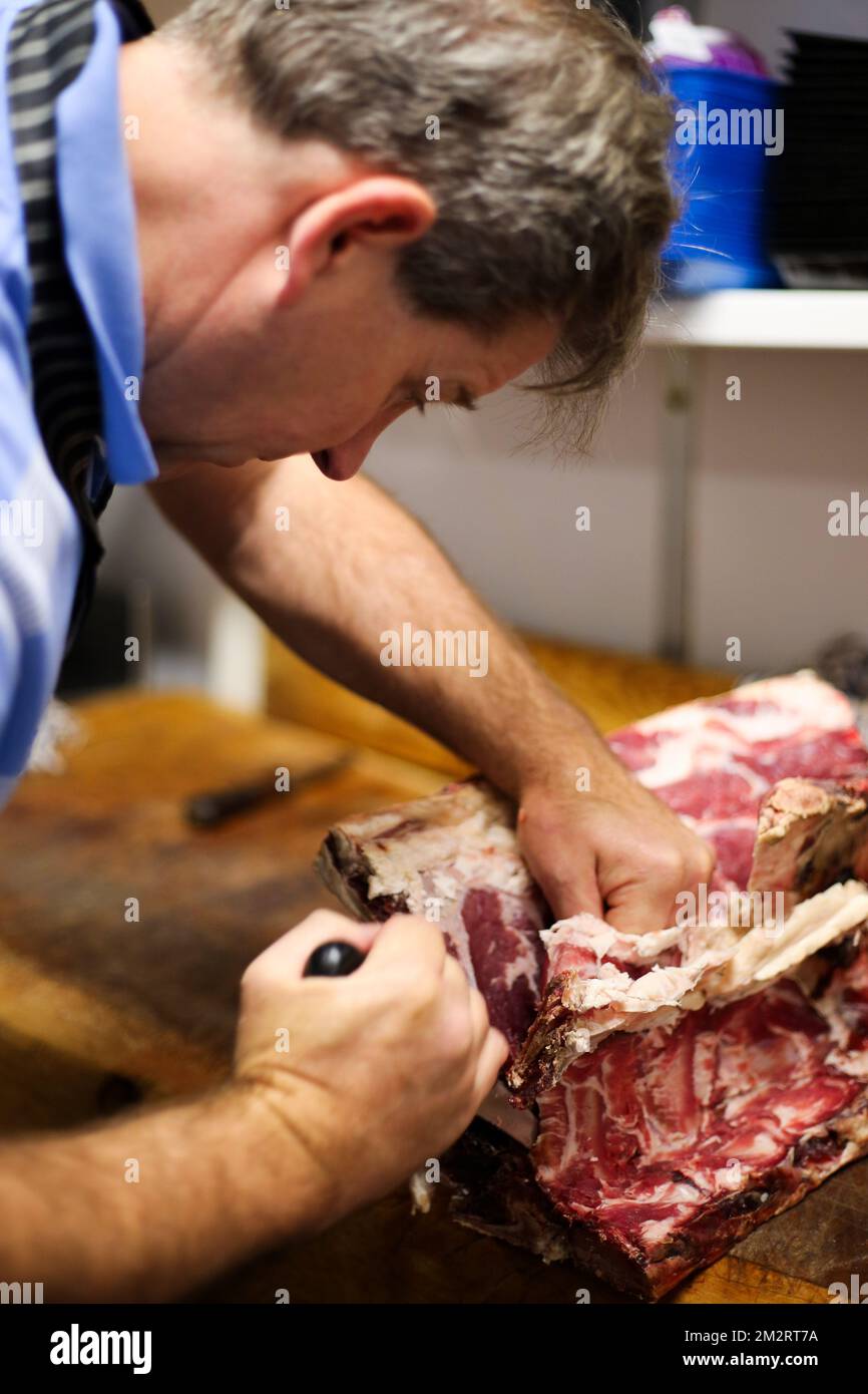 Ein Metzger bei der Arbeit, der eine Rippe Rindfleisch in einem traditionellen Metzgerladen in Salisbury UK 2022 entbeint. Stockfoto