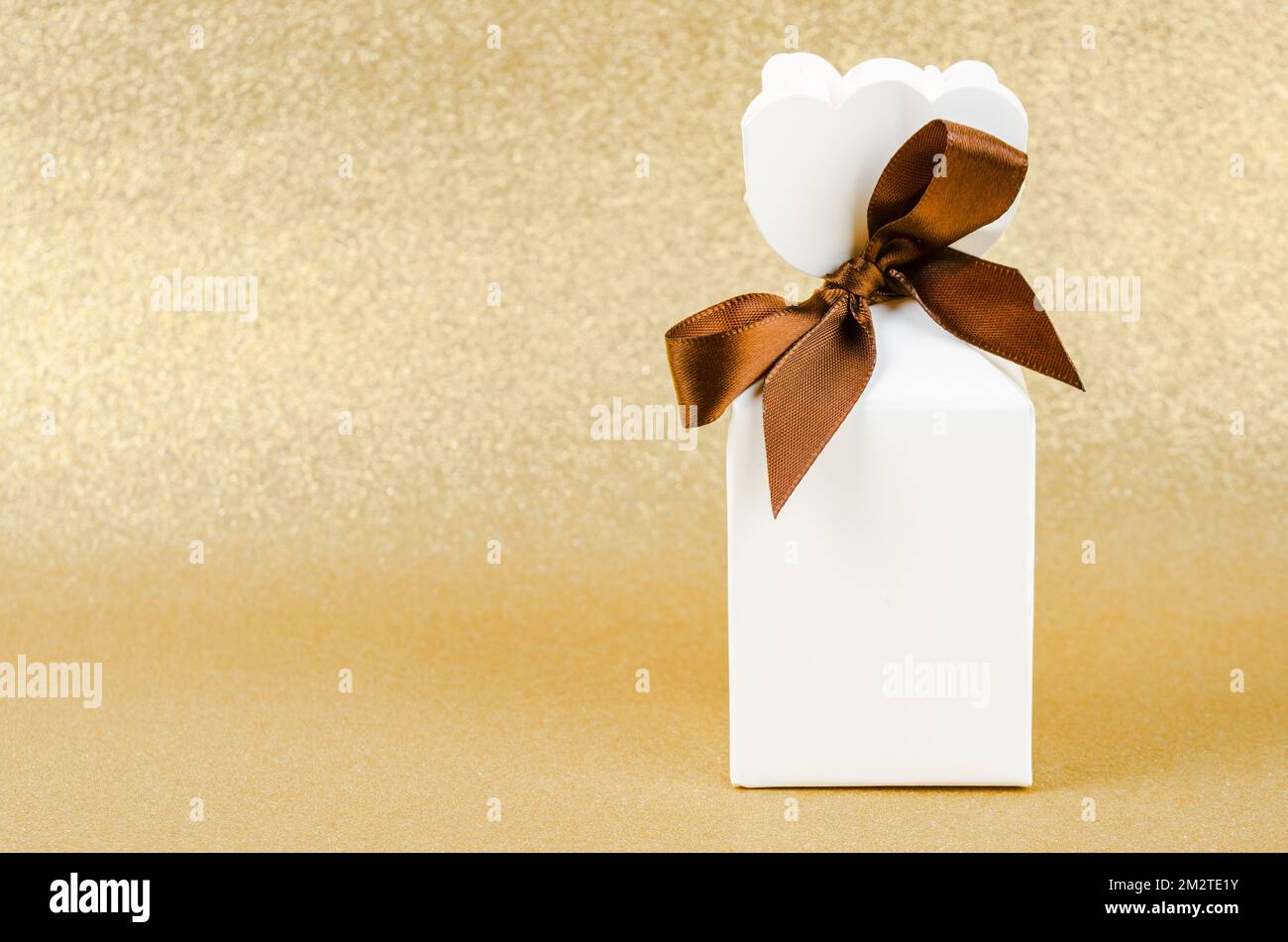 Geschenkbox mit braunem Band auf goldenem Glitzer-Struktur-weihnachtshintergrund. Stockfoto