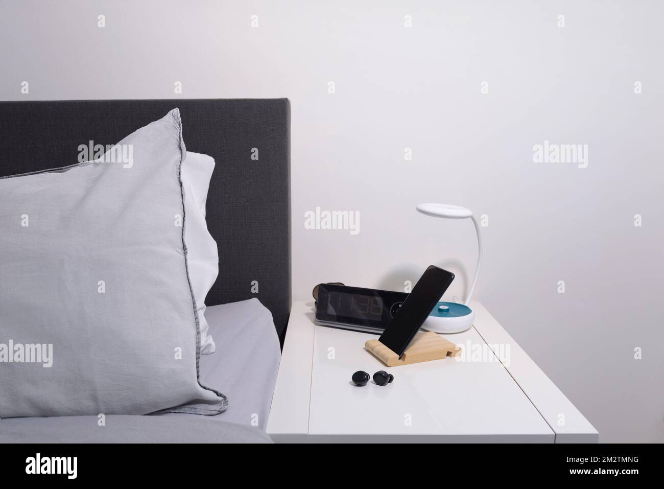 Schlafzimmer-Akten. Smartphone auf dem Nachttisch mit Lampe, Headset, Uhr und Bett. Stockfoto