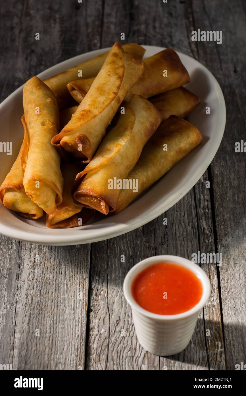 Hausgemachte Frühlingsrollen mit süßer und saurer chinesischer Sauce. Auf einer weißen Platte auf einem Holzhintergrund Stockfoto