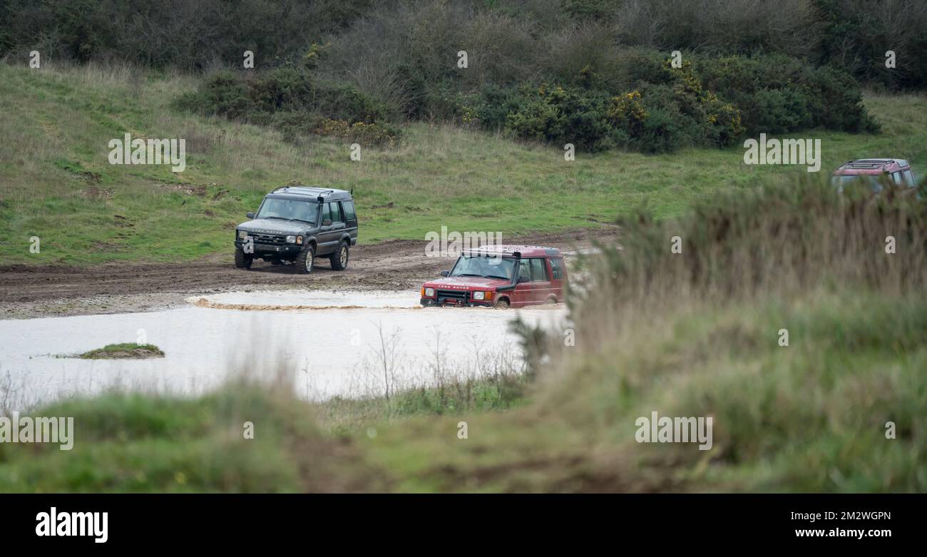 Zwei Land Rover Discovery 4x4 Geländefahrzeuge, die durch tiefes Wasser und Schlamm auf offener Landschaft in Wiltshire UK gefahren werden Stockfoto