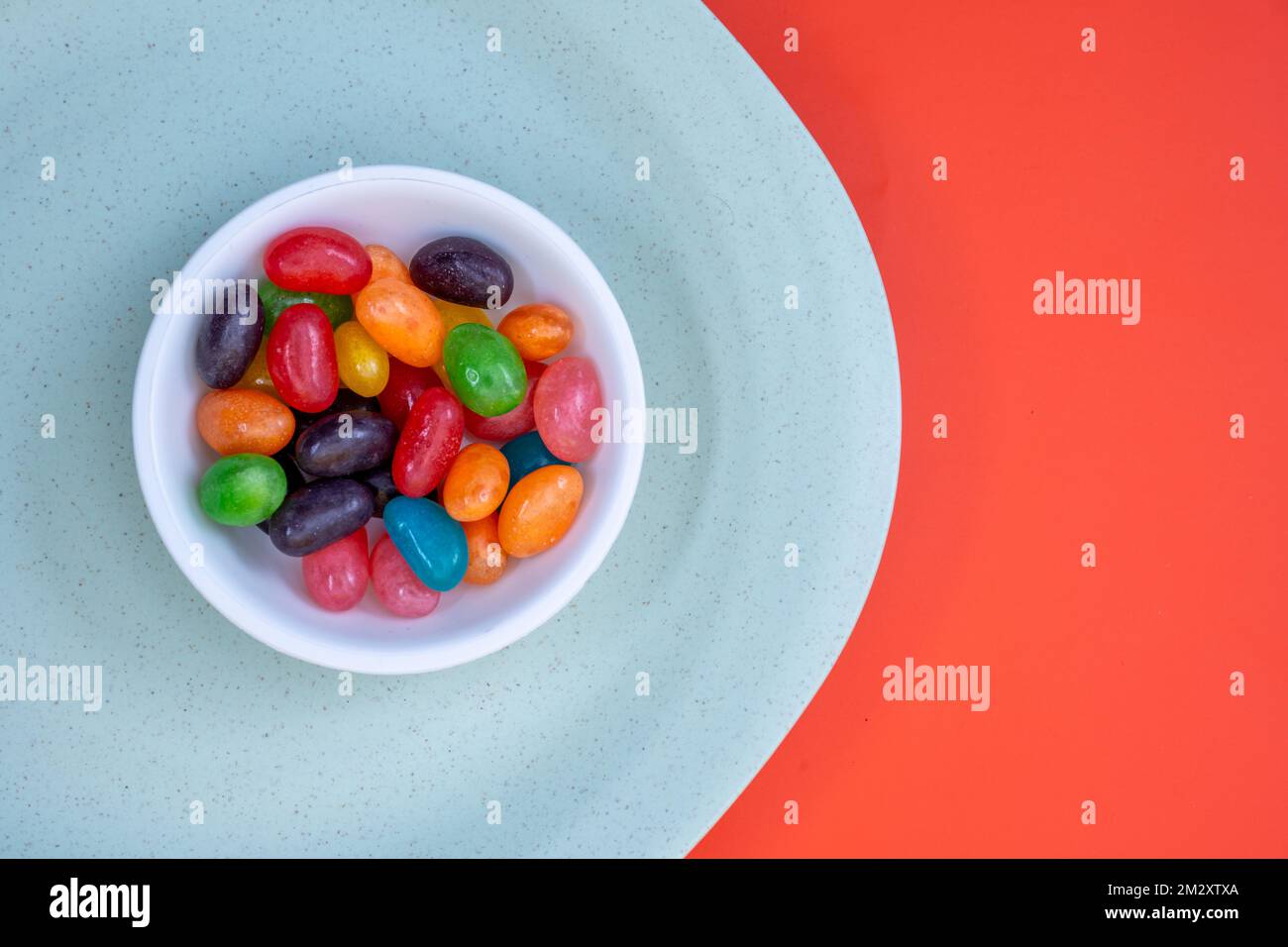 Schüssel voll mit farbigen Jelly Bean Sweets auf grünem und orangefarbenem Hintergrund Stockfoto