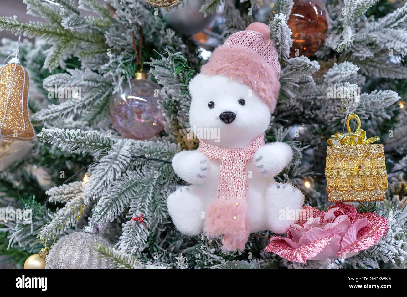 Weiches, spielzeugisches Eisbärchen mit Strickmütze und Schal am Weihnachtsbaum. Stockfoto