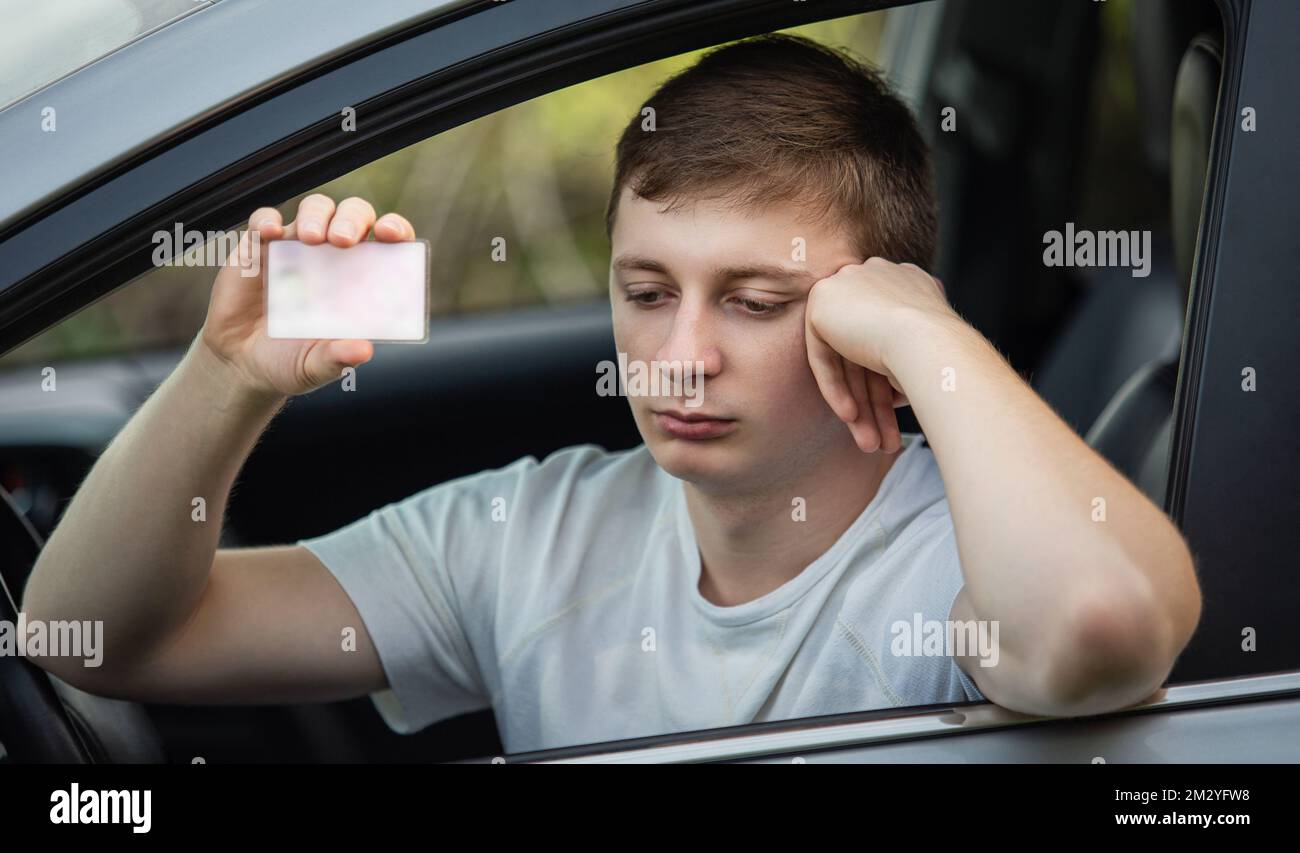 Verärgerter Fahrer, der seinen Führerschein aus dem Autofenster zeigt, wie bei der Polizeikontrolle. Fahrunsicherheit bei Nichtbeachtung der Verkehrsvorschriften Stockfoto