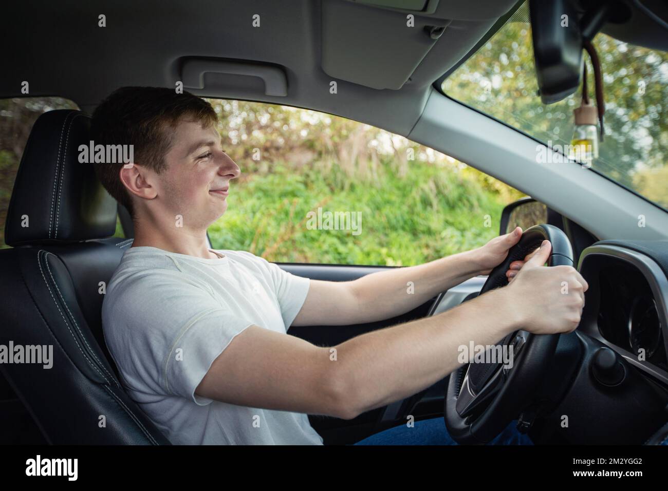 Stolzer und fröhlicher junger Fahrer vor dem Lenkrad, der sein neues Auto selbstbewusst fährt Stockfoto
