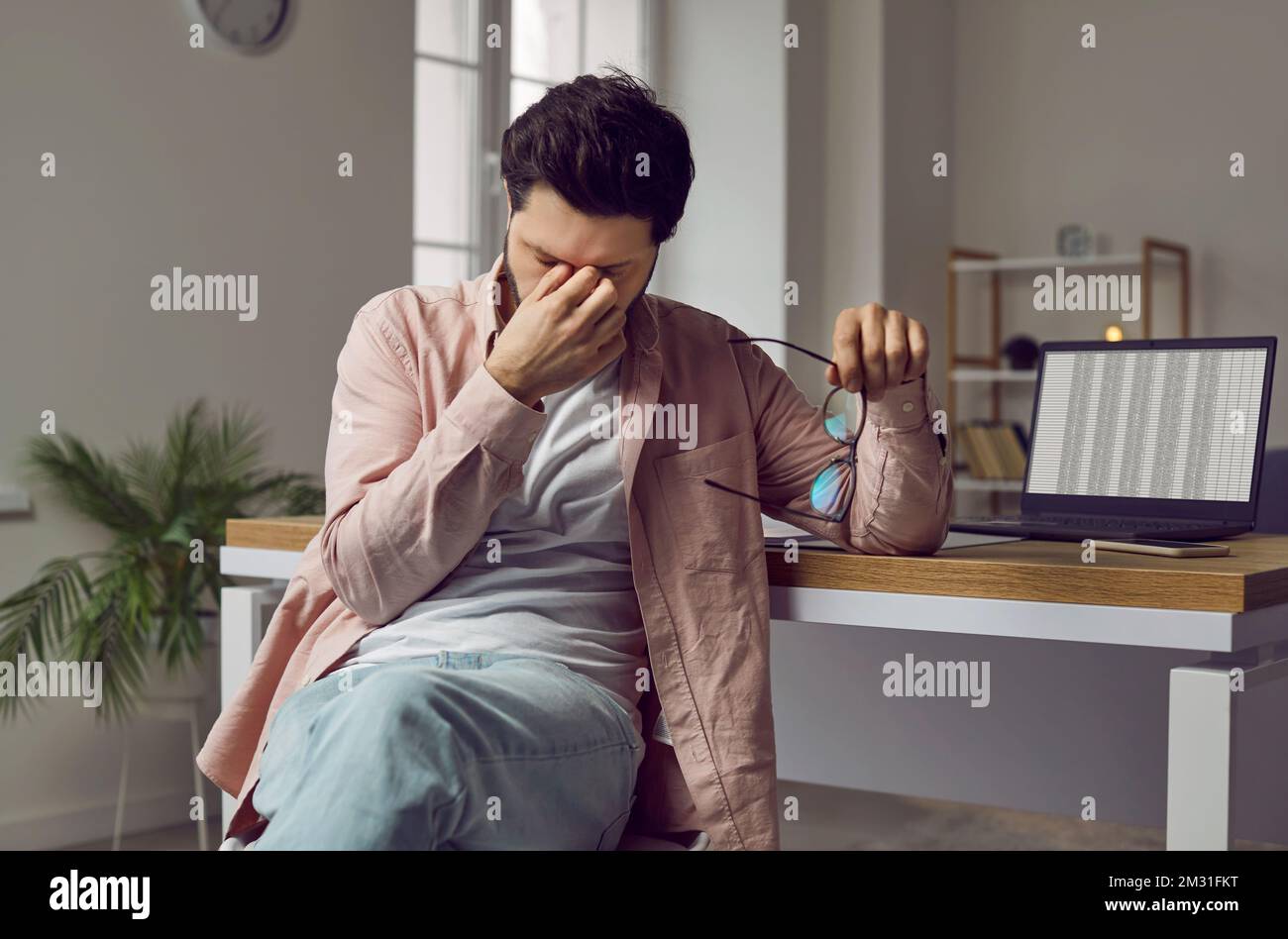 Müder, gestresster Mann mit anstrengenden Augen, der mit einem Laptop am Schreibtisch sitzt Stockfoto