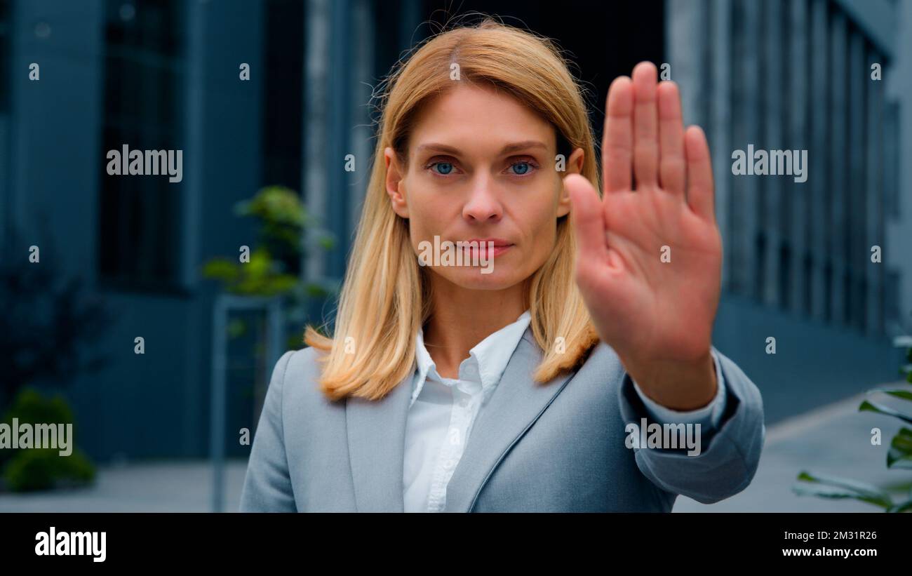 Eine ernsthafte Frau, die draußen steht und in die Kamera schaut, mit Stoppgesten, die Hand vor sich hält selbstbewusste Geschäftsfrau, die persönliche Grenzen schützt Stockfoto