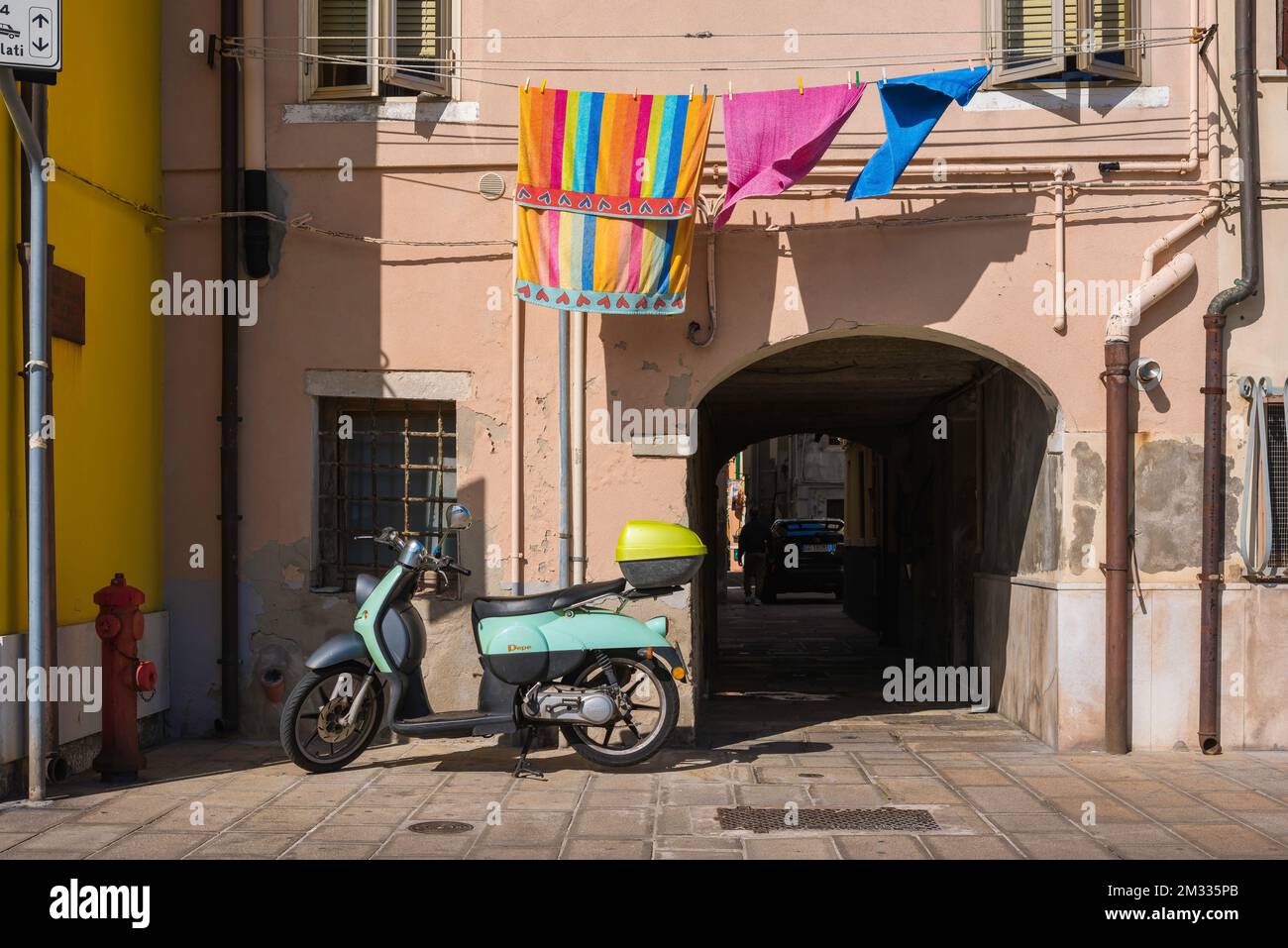 Street Italy, im Sommer Blick auf einen Roller, der an einer rosafarbenen Mauer geparkt ist und über der eine farbenfrohe Wäsche hängt, Chioggia, Comune of Venice, Veneto, Italien Stockfoto