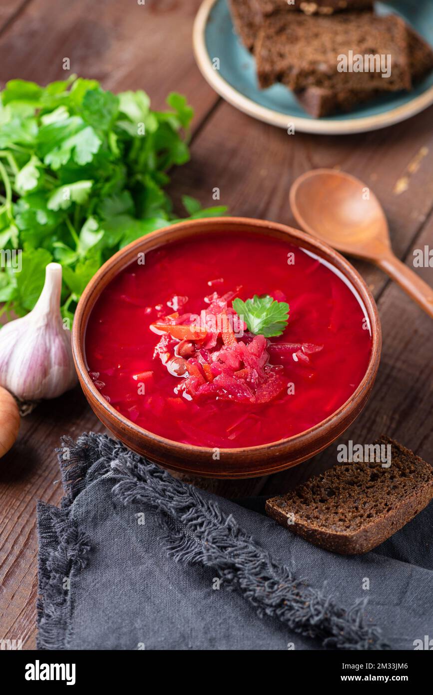 Vegetarischer Borscht serviert mit dunklem Roggenbrot in der Schüssel auf Holztisch. Ukrainische Küche. Rote-Bete-Gemüsesuppe Stockfoto