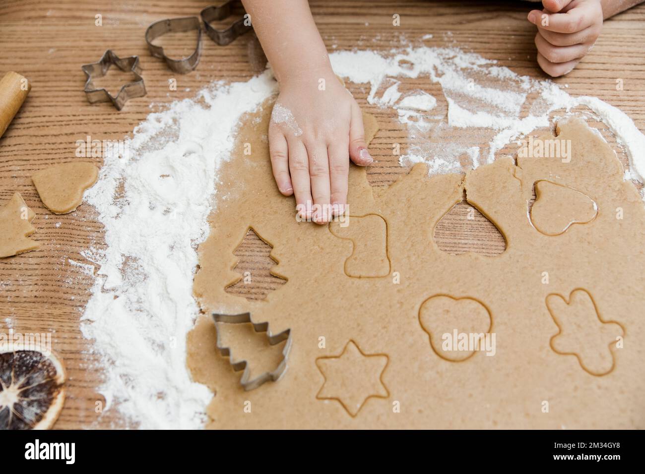 Das kleine Mädchen bereitet Lebkuchen in der Küche zu. Blick von oben. Kleine Hände mit Schinken und Mehl, Keksschneider, Gewürz auf dem Holztisch. Stockfoto