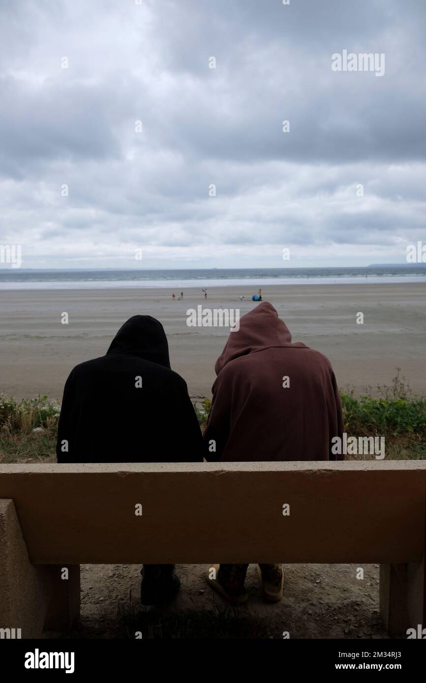 Zwei Teenager in Kapuzenpullis auf einer Bank am Meer Stockfoto