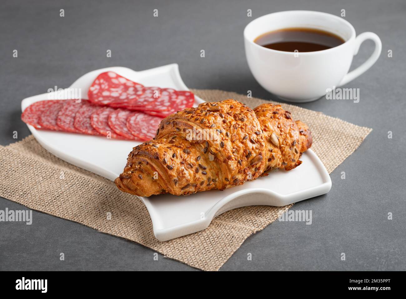 Frisches Croissant-Sandwich mit Wurst und Kaffee auf grauem Tisch Stockfoto