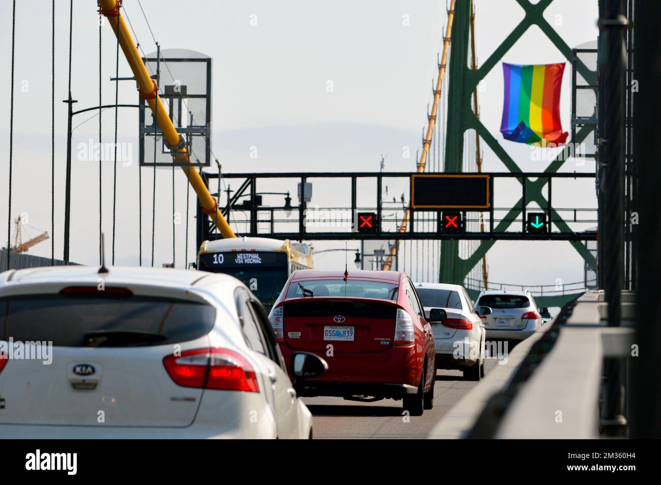 Autos auf der Angus L. Macdonald Bridge in Halifax, Nova Scotia, Kanada, mit der LGBT Pride Flag, die von einem der Brückentürme hängt. Stockfoto