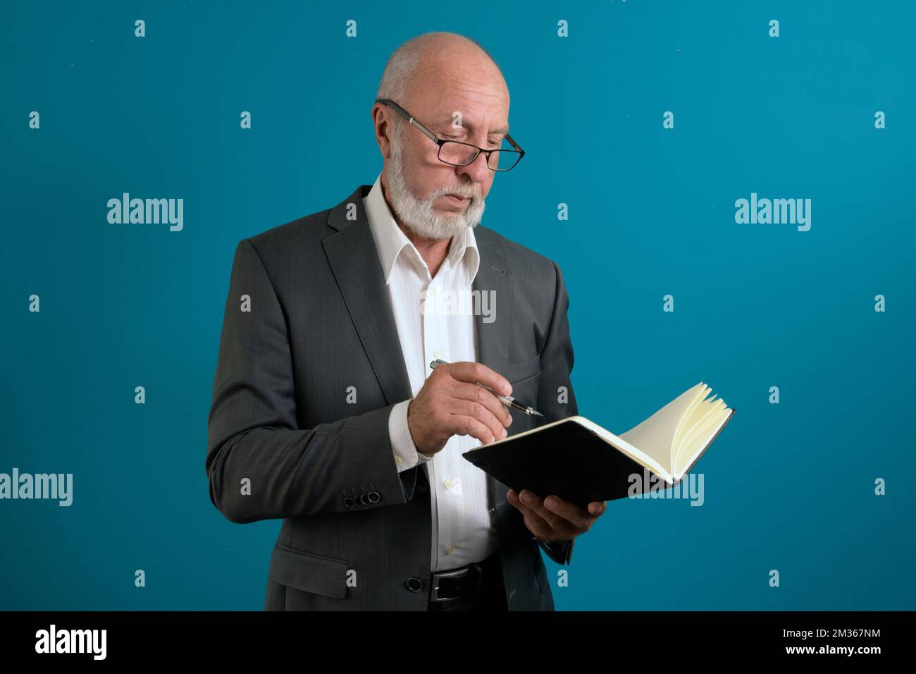 Ein älterer Mann im Anzug mit Notizbuch und Stift denkt über eine Aufgabe nach. Auf blauem Hintergrund Stockfoto