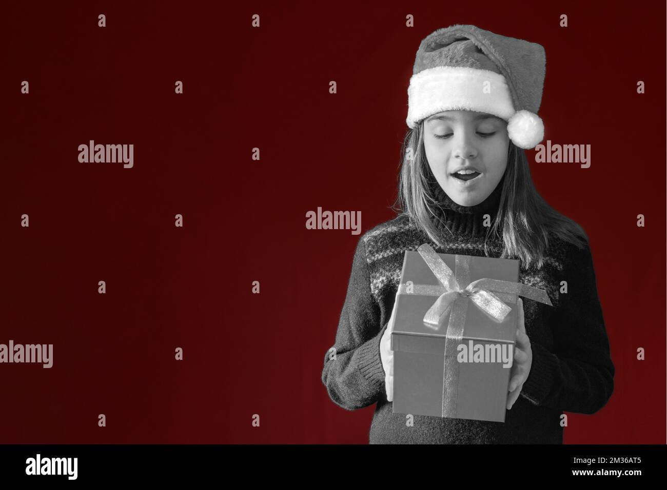 Weihnachtsbanner mit Teenager in weihnachtsmannmütze und Geschenkbox. Dunkelroter Hintergrund für Farb- und schwarzweißkonzept. Platz für Text Stockfoto