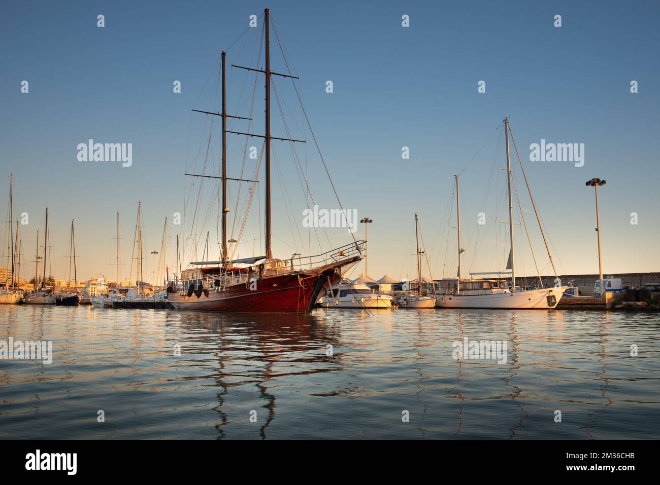 Ein hölzernes Segelschiff mit zwei Masten liegt im Hafen von Mazara del Vallo vor Anker. Außerdem gibt es viele andere Segelschiffe im Wasser, die illumina sind Stockfoto