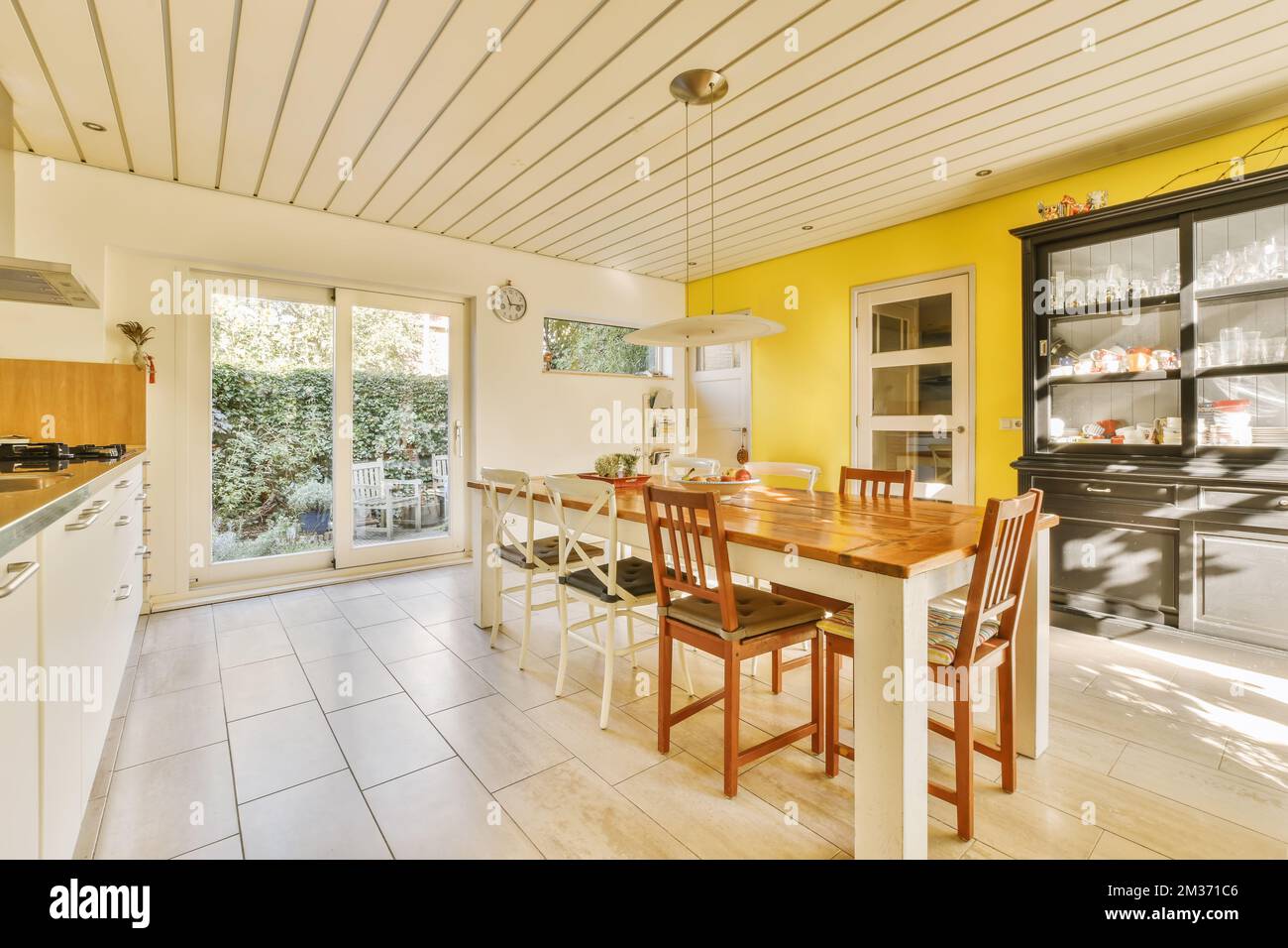 Küche und Essbereich in einem Haus mit weißen Fliesen auf dem Boden, gelb bemalten Wänden und Decken Stockfoto