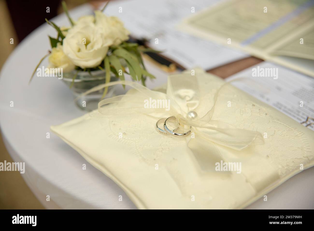Zwei Platinringe für die Hochzeit liegen auf einem Seidenspitzenkissen für Ringe. Hochzeitszubehör Braut und Bräutigam, bevor die Zeremonie auf einem weißen Tisch fotografiert wurde Stockfoto