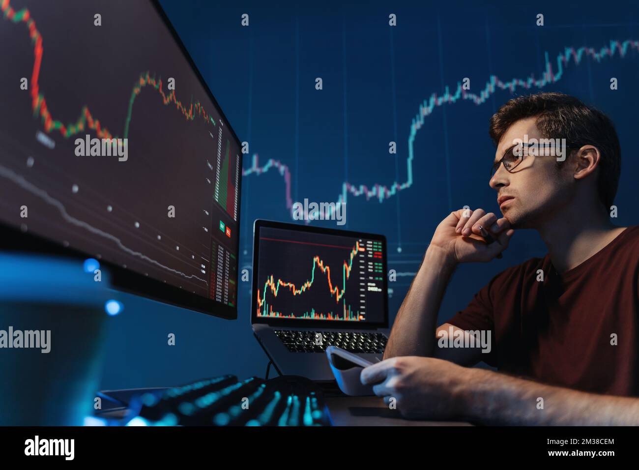 Ein seriöser Kryptohändler, der auf den Bildschirm schaut, mit Kerzenhalter, Stift und Notizblock in der Hand hält, Notizen macht, die Risiken des Handels mit Kryptowährung unter den Bedingungen der globalen Finanzkrise analysiert Stockfoto