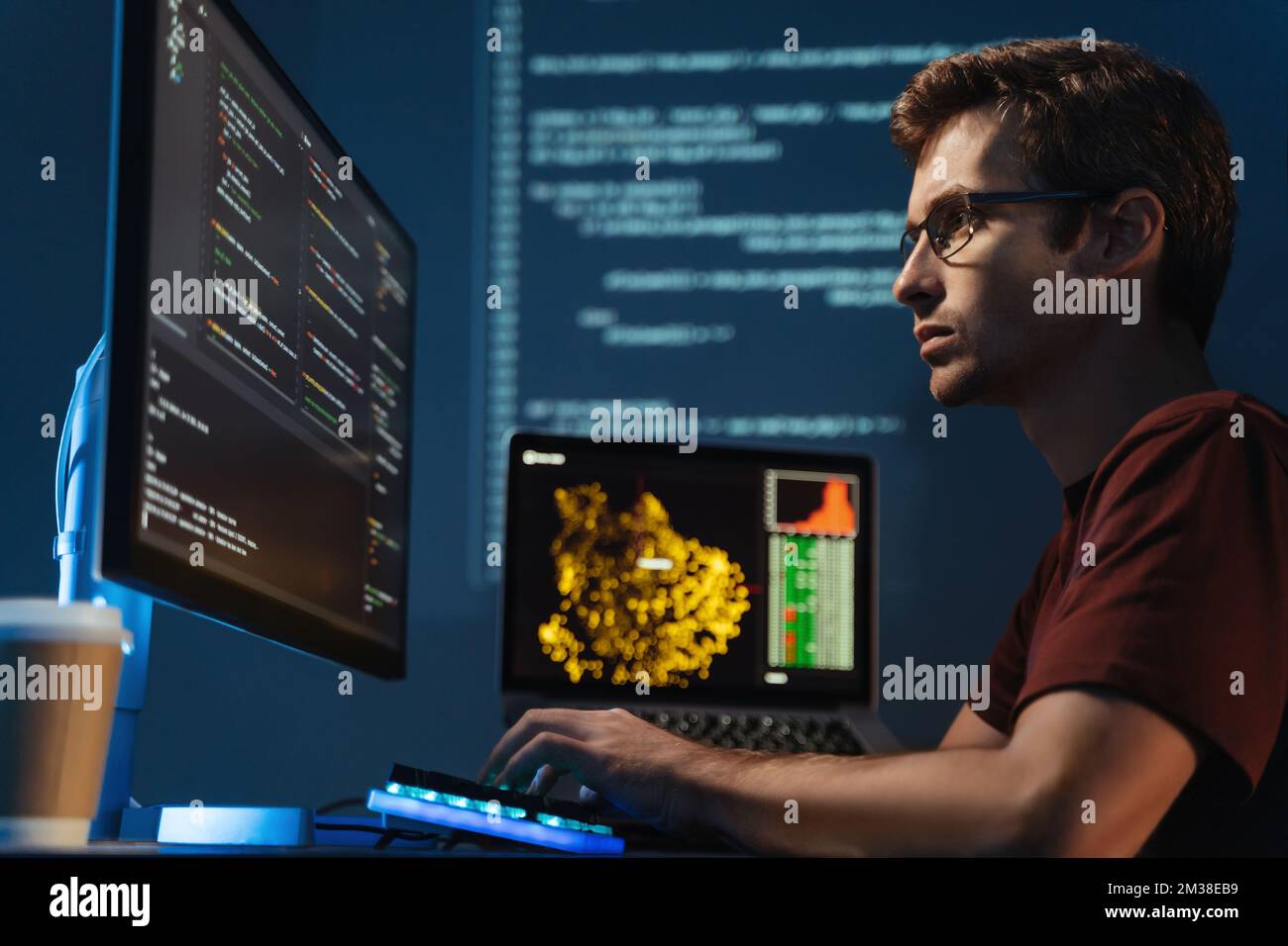 Seitenansicht eines intelligenten Programmierers, der auf einen großen Monitor schaut, die id-Adresse und das Debugging-System überprüft, HTML-Code schreibt, bis spät in der Nacht am Tisch sitzt und einen gezoomten digitalen Hintergrund betrachtet Stockfoto