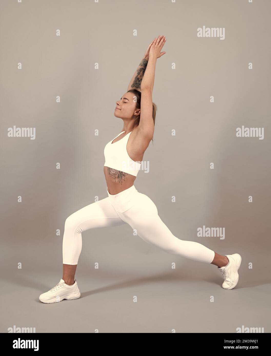 Frau in Sportbekleidung beim Stretching. Mädchen, die sich vor dem Training auf grauem Studiohintergrund ausstrecken. Stockfoto