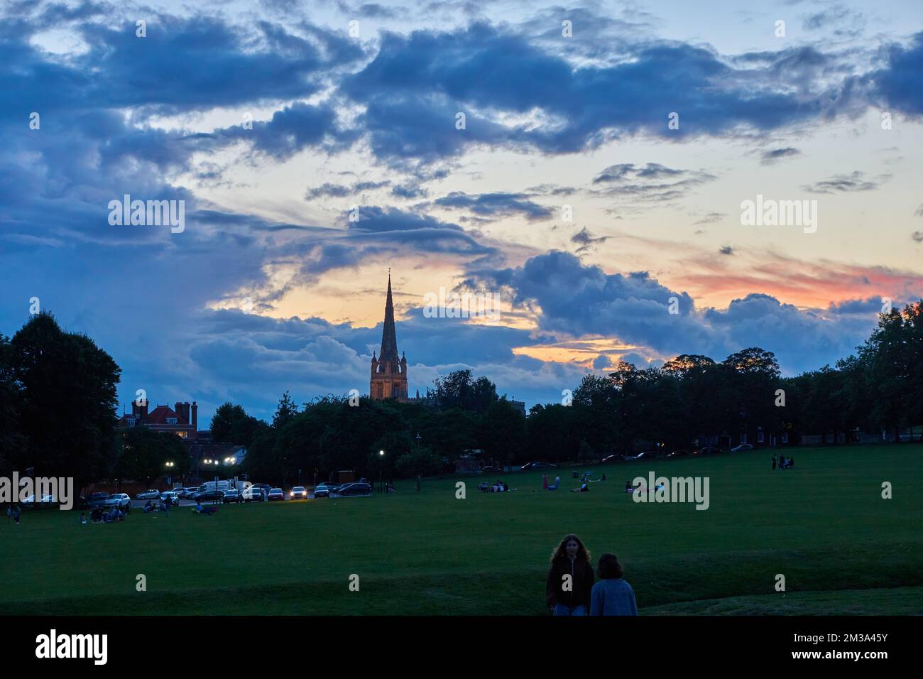 Menschen auf dem Gras in der Dämmerung am Gemeindehaus mit dem Kirchturm im Hintergrund in Saffron Walden, Essex, Großbritannien Stockfoto