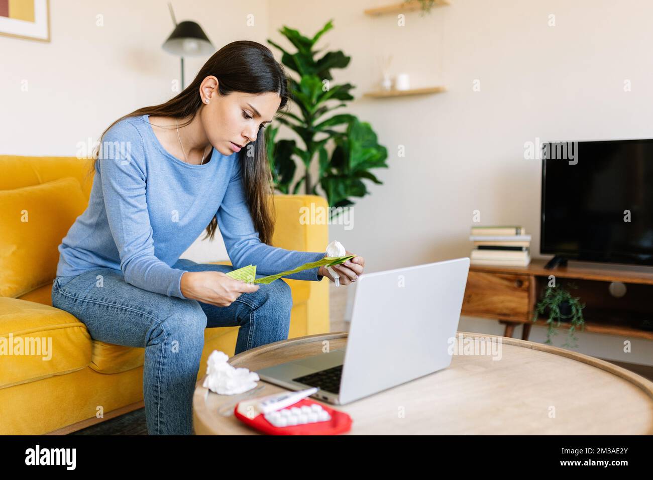 Junge kranke Frau liest Medikamentenanweisungen, während sie zu Hause auf dem Sofa sitzt Stockfoto