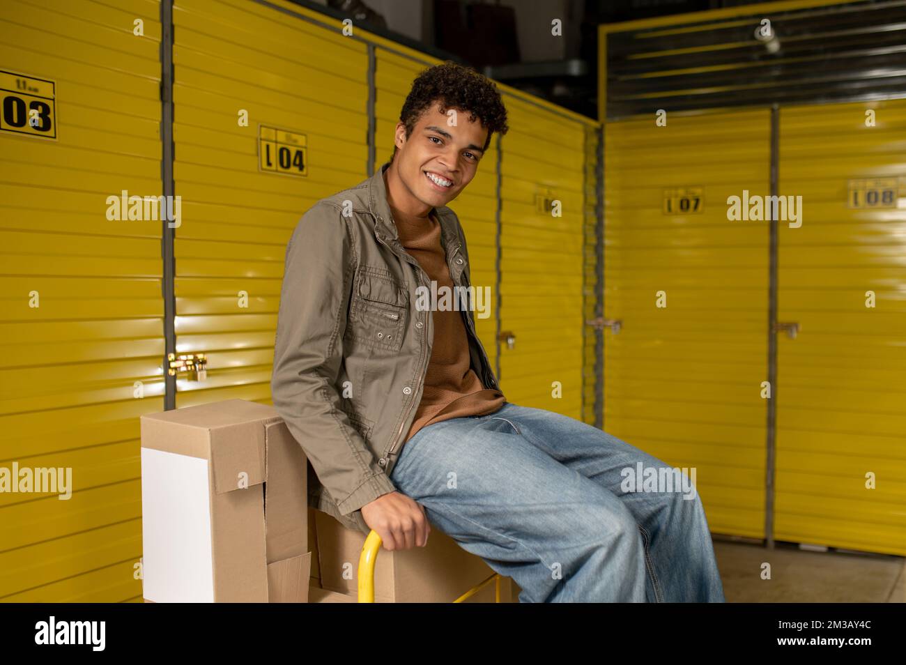 Lächelnder junger Lagerarbeiter, der auf der Kiste sitzt und sich ausruht Stockfoto