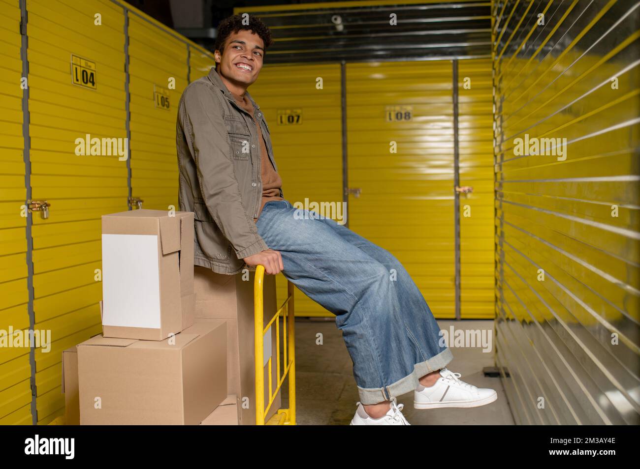 Lächelnder junger Lagerarbeiter, der auf der Kiste sitzt und sich ausruht Stockfoto