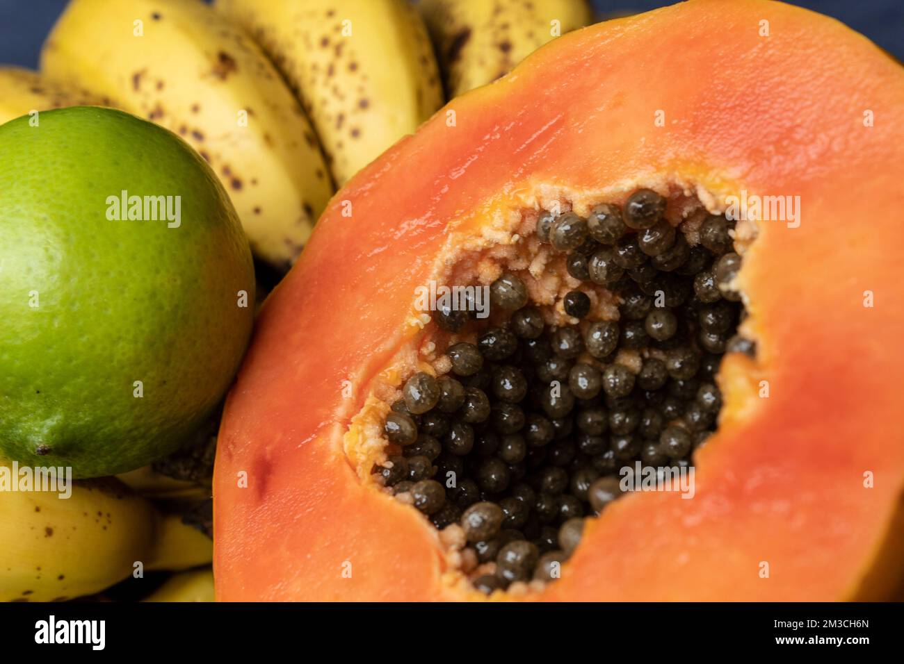 Aus nächster Nähe sehen Sie eine frisch geschnittene Orangenpapaya mit Samen im Inneren, Sommersprossen und Zitronen im Hintergrund. Obst- und Esskonzeptsfotografie Stockfoto