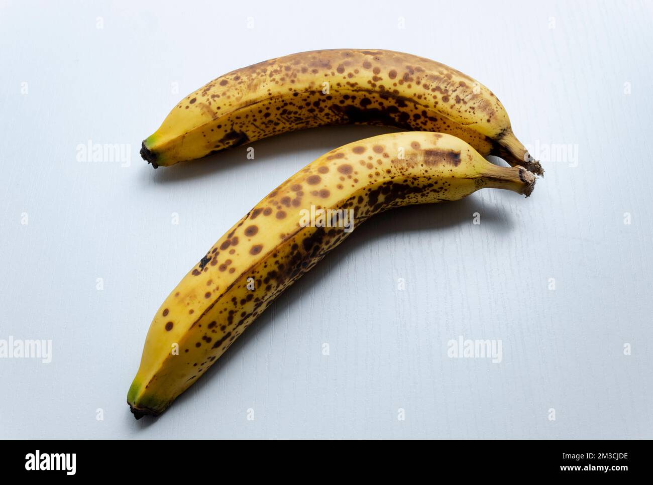 Nahaufnahme zu zwei gelben Sommersprossen Bananen in diagonaler Form über einem weißen Holztisch. Stockfoto