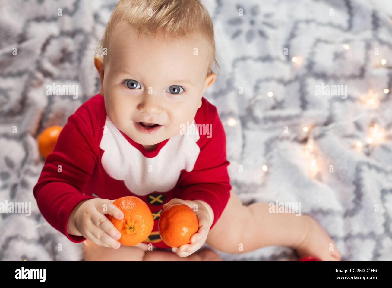 Neujahrsbaby im weihnachtsmannkostüm mit Mandarinen Stockfoto