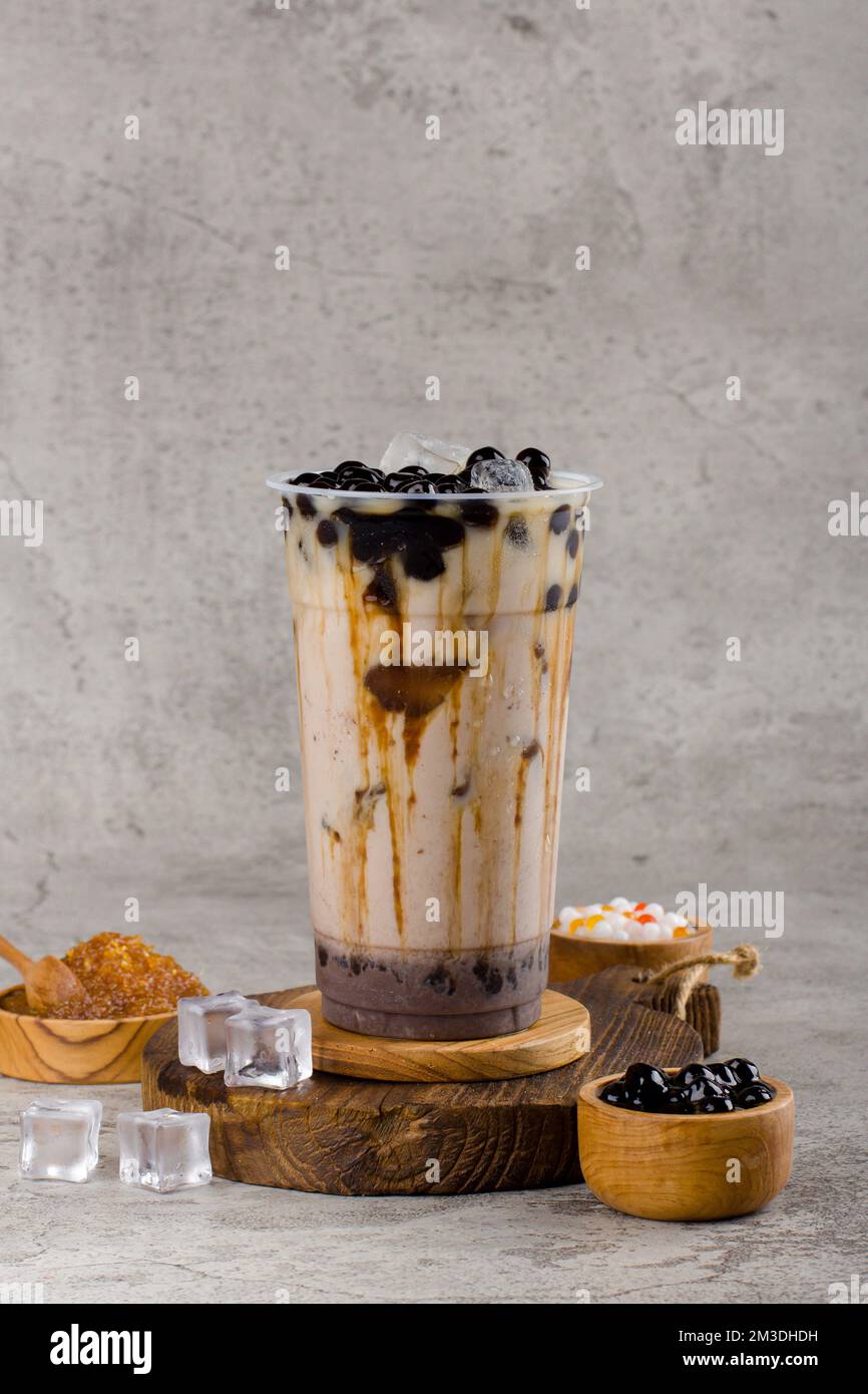 Boba- oder Tapioka-Perlen sind taiwanesischer Seifenmilchtee in Plastikbecher mit Kaffee-Latte-Aroma auf texturiertem Hintergrund, Sommererfrischung. Stockfoto