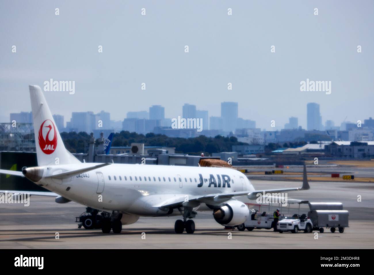 Tokio, Japan - 9. November 2022: Japan Airlines fliegt auf Asphalt mit Hilfsfahrzeugen und Skyline der Stadt durch Dunst sichtbar Stockfoto