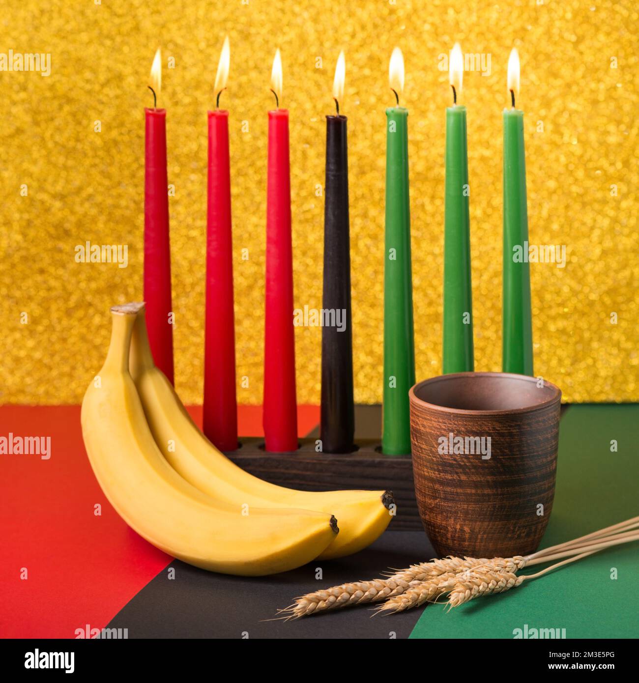 Afrikanisches Kwanzaa-Urlaubskonzept mit traditionellen Kerzen, Banane, Schüssel und Weizenohren Stockfoto