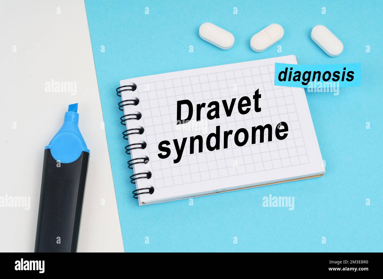 Medizin und Gesundheitskonzept. Auf einer weißen und blauen Oberfläche sind Pillen, ein Marker und ein Notizbuch mit der Inschrift "Dravet-Syndrom", ein Aufkleber mit dem Stockfoto