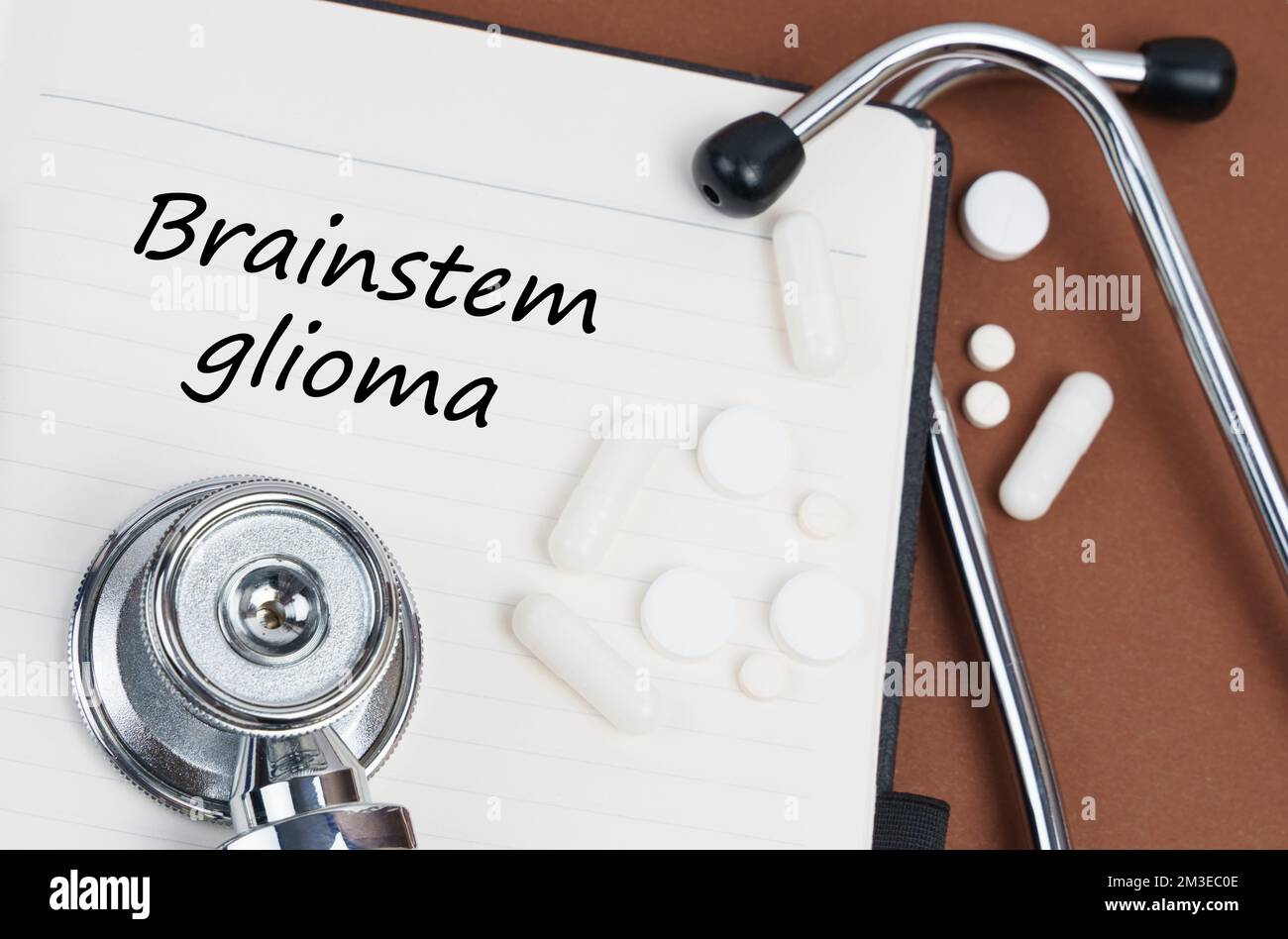 Medizin und Gesundheitskonzept. Auf einer braunen Oberfläche liegen Pillen, ein Stethoskop und ein Notizbuch mit der Inschrift "Brainstem Glioma" Stockfoto