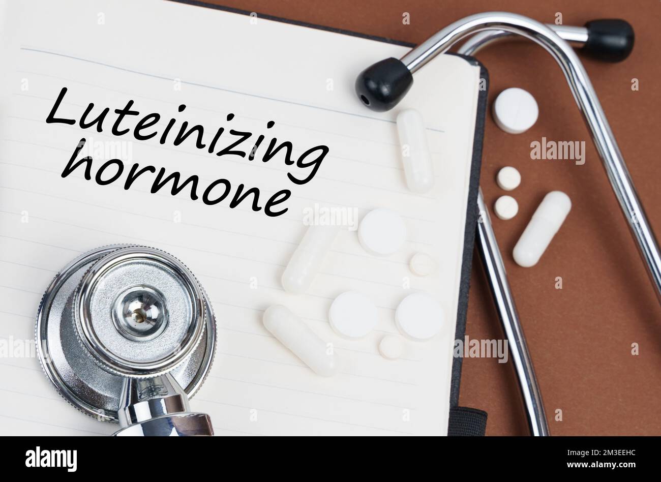 Medizin und Gesundheitskonzept. Auf einer braunen Oberfläche liegen Pillen, ein Stethoskop und ein Notizbuch mit der Aufschrift "Luteinisierendes Hormon" Stockfoto