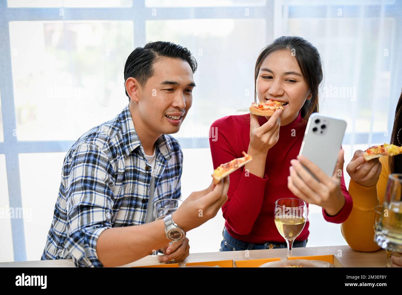 Glückliche und fröhliche asiatische Frau, die Selfie mit ihrem Handy macht, während sie Pizza auf der Party mit ihren Freunden isst. Neujahrsparty, Firmenfeier, pi Stockfoto