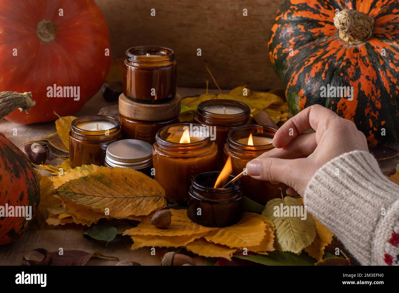 Leichte Sojakerzen brennen in Glasgläsern. Baumblätter, Kürbis. Komfort zu Hause. Kerze in einem braunen Glas. Duft und Licht. Duftkerze von Hand. Aromatherapie. Herbststimmung. Gemütliches Dekor im Herbst. Stockfoto