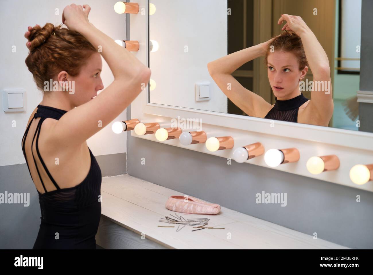 Junge Ballerina, die ihr Haar mit haarnadeln in ein Brötchen frisiert. Stockfoto