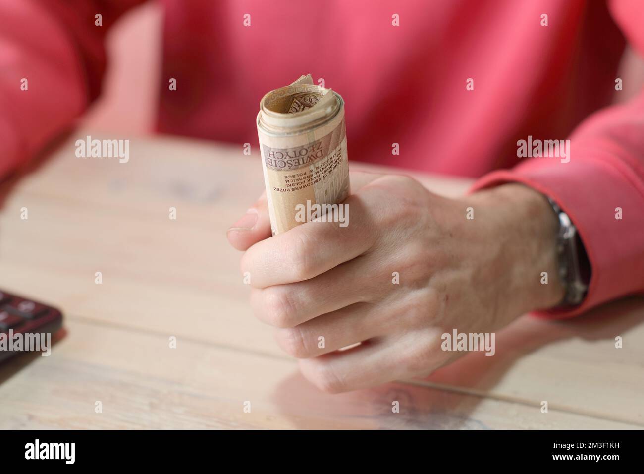 Eine Rolle polnischer Zloty-Banknoten in der Hand einer Person in einem roten Sweatshirt über dem Tisch Stockfoto