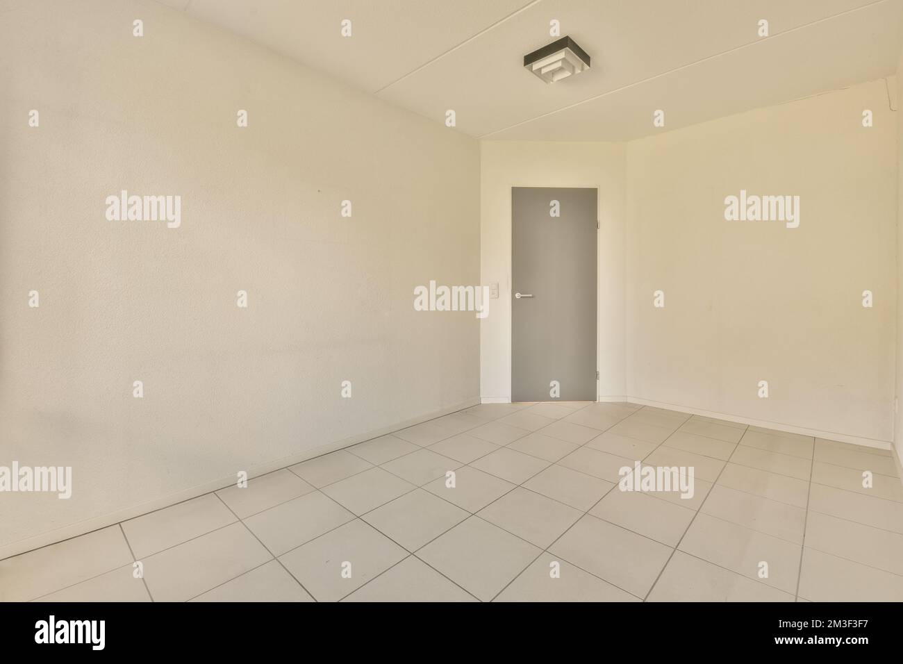 Ein leerer Raum mit weißen Wänden und Fliesenboden in der Mitte des Zimmers, es gibt keine einzige Tür Stockfoto