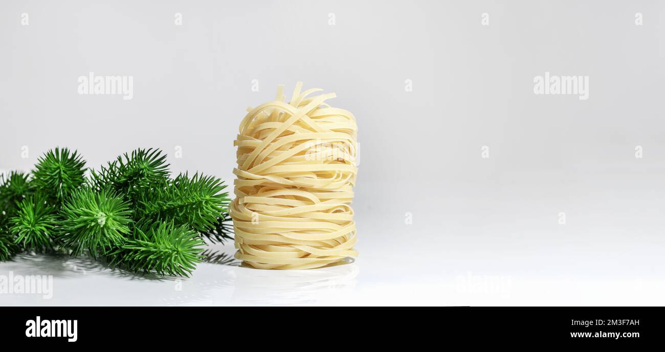 Italienische Weihnachtspasta. Spaghetti Capellini, in Form eines Turms, isoliert auf weißem Hintergrund mit harten Schatten und Reflexion, neben dem Chr Stockfoto