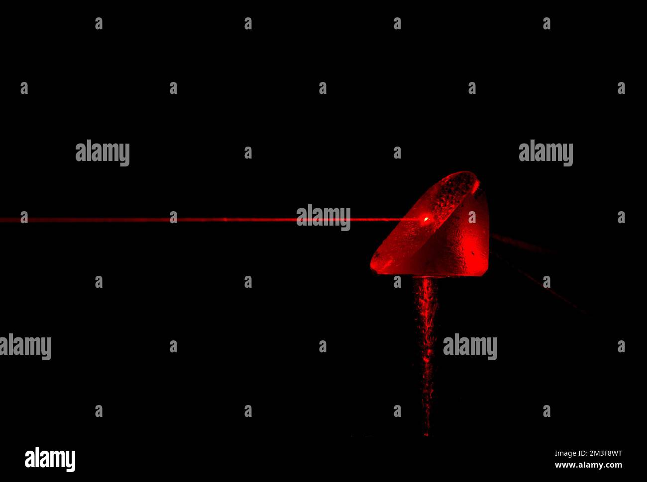 Ein roter Laserstrahl trifft auf ein Prisma. Der Strahl wurde durch einen feinen Wasserstrahl sichtbar gemacht. Wassertropfen auf dem Prisma und Wasserstreifen im Strahl. Stockfoto