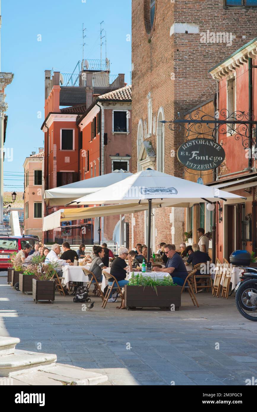 Speisen und Getränke aus Chioggia, im Sommer sehen Sie eine Gruppe von Menschen, die außerhalb einer Pizzeria im malerischen Hafen von Chioggia, Comune of Venice, Italien, essen Stockfoto